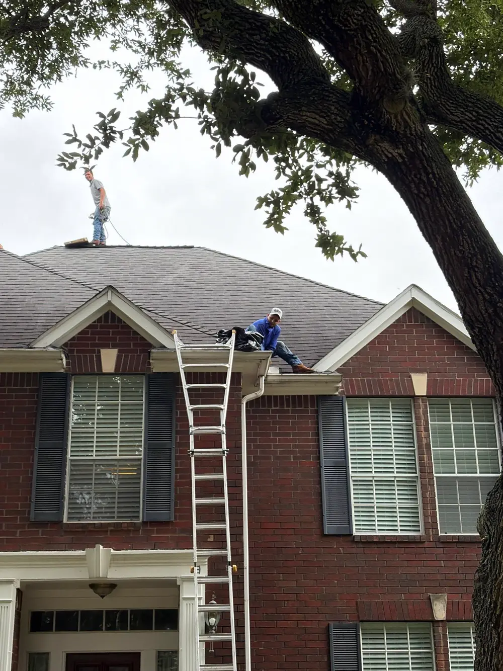 Roofer on a ladder inspecting a two-story brick home in Sugar Land, TX